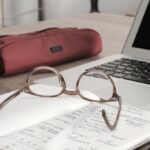 glasses on a notebook near a computer and cell phone
