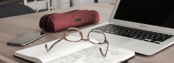 glasses on a notebook near a computer and cell phone