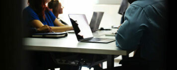 group of students with laptops open looking at a speaker/professor