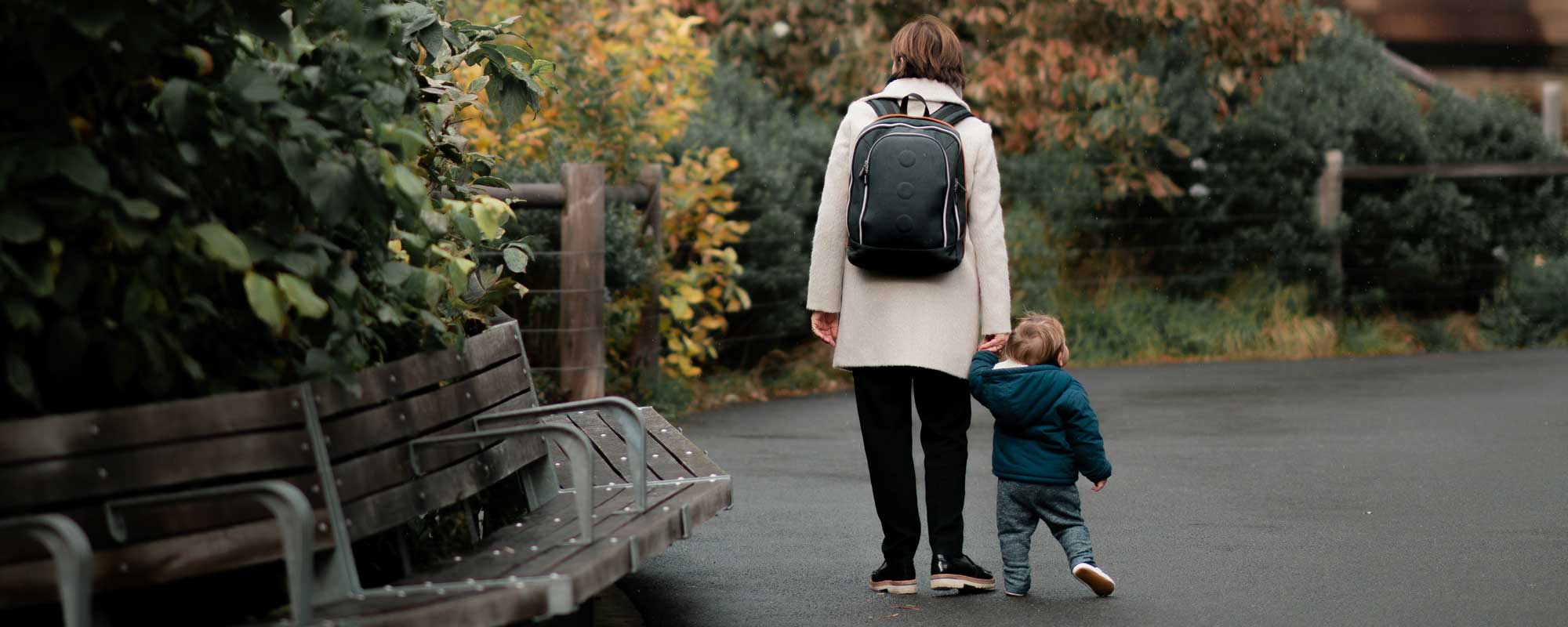 parent a mother walking with her toddler, she is wearing a backpack implying she is a student