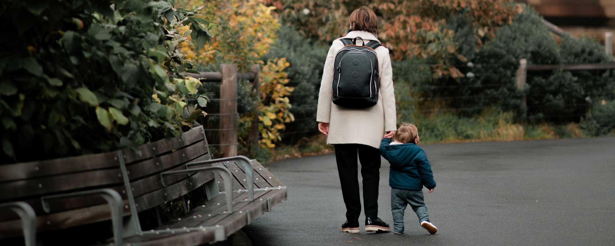 a mother walking with her toddler, she is wearing a backpack implying she is a student