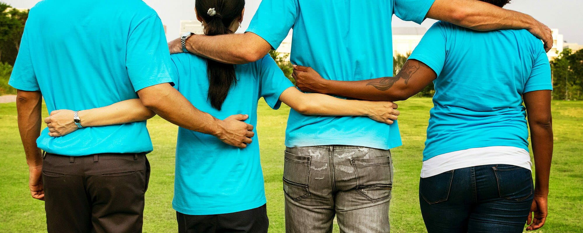 four diverse students standing with their arms linked on each others' backs to symbolize a team