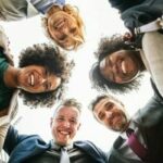 group of diverse students looking down at the camera and smiling. their heads form a circle