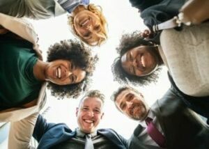 group of diverse students looking down at the camera and smiling. their heads form a circle