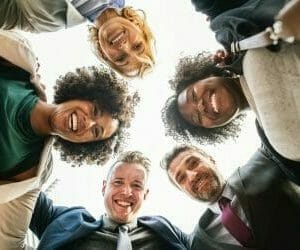 group of diverse students looking down at the camera and smiling. their heads form a circle