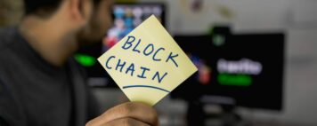 What is blockchain? An image of a man at a computer holding up a sign reading "Blockchain"