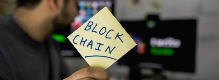 What is blockchain? An image of a man at a computer holding up a sign reading "Blockchain"