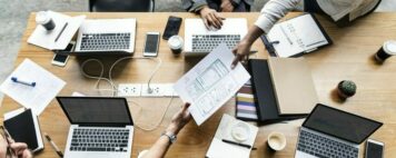 People sitting around a table with laptops in front of them while a paper is passed around