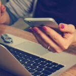 Image of a student holding a phone, at a laptop