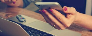 Image of a student holding a phone, at a laptop