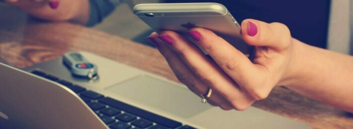 Image of a student holding a phone, at a laptop