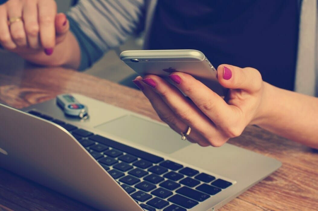Image of a student holding a phone, at a laptop