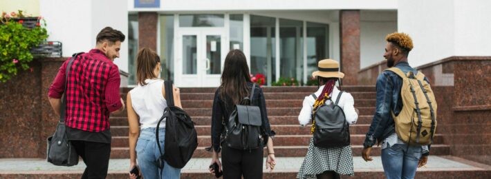 The backs of 5 students walking towards a building together.