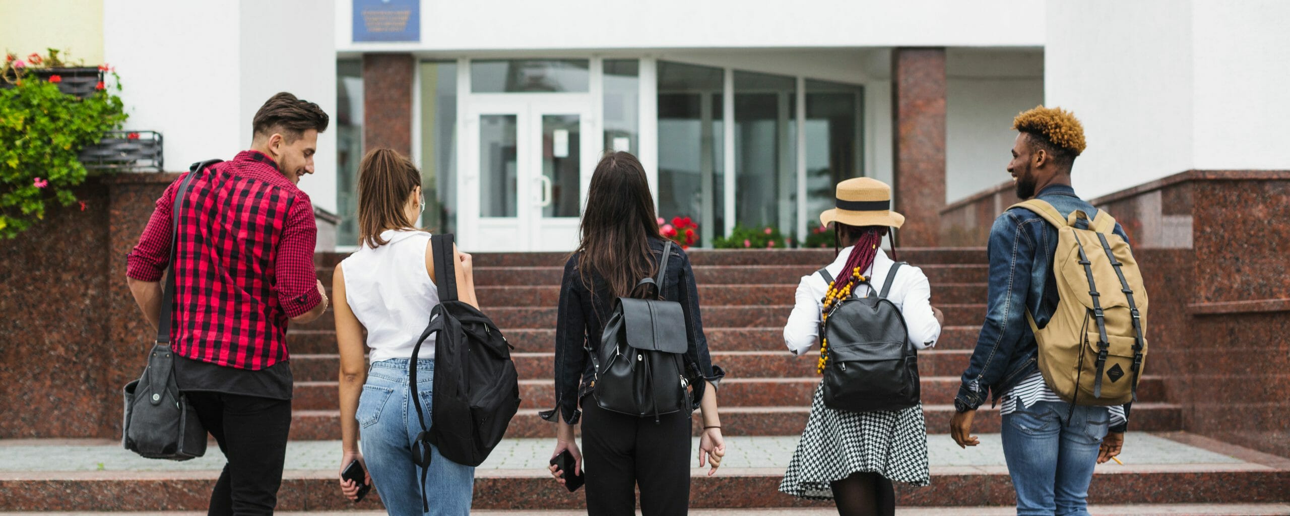 The backs of 5 students walking towards a building together.