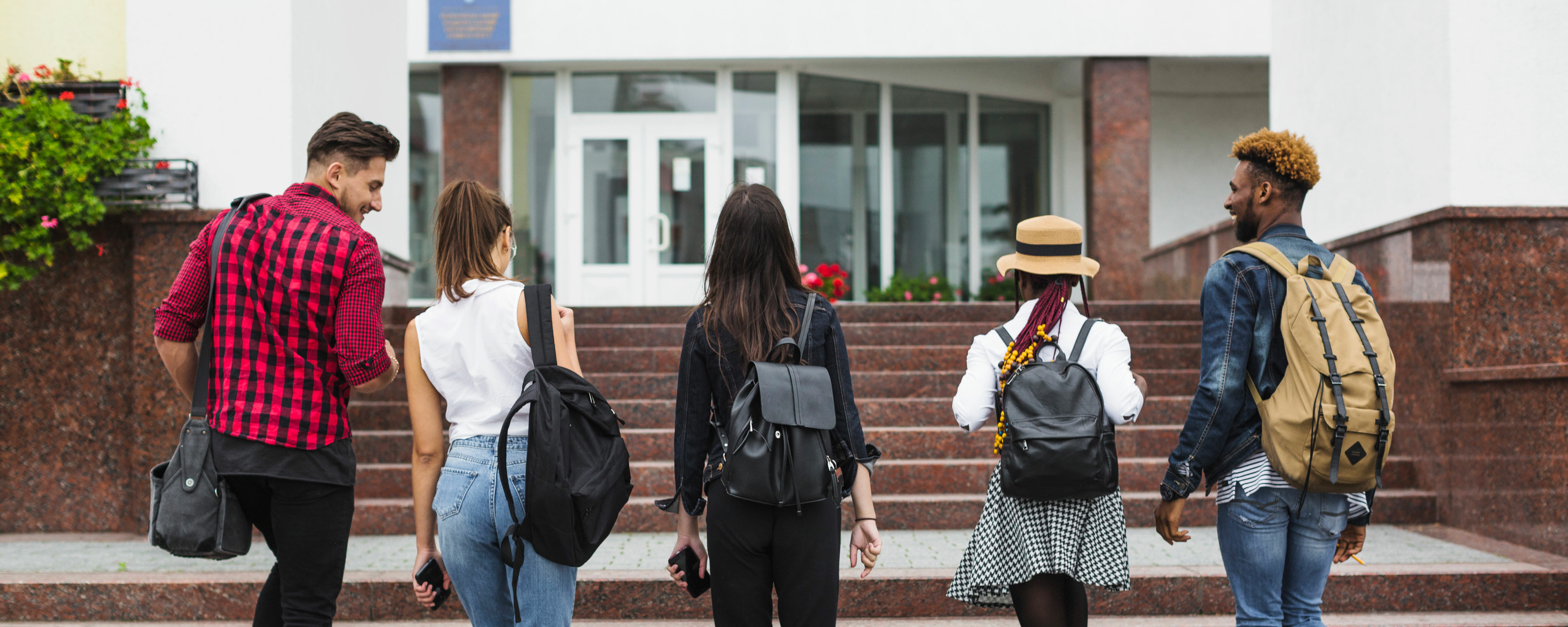 diverse-students The backs of 5 students walking towards a building together.