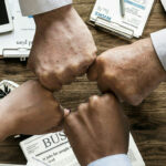 4 people fist-bumping across a table strewn with meeting materials.