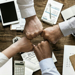 4 people fist-bumping across a table strewn with meeting materials.
