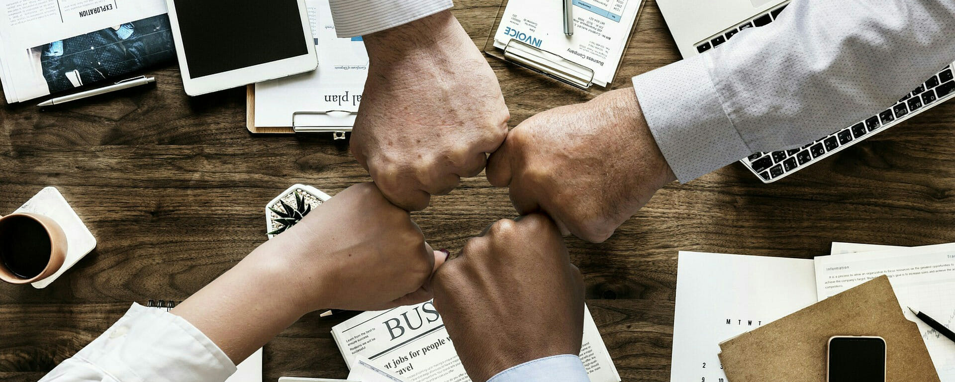 4 people fist-bumping across a table strewn with meeting materials.