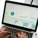 A person working on a laptop reviewing graphs.