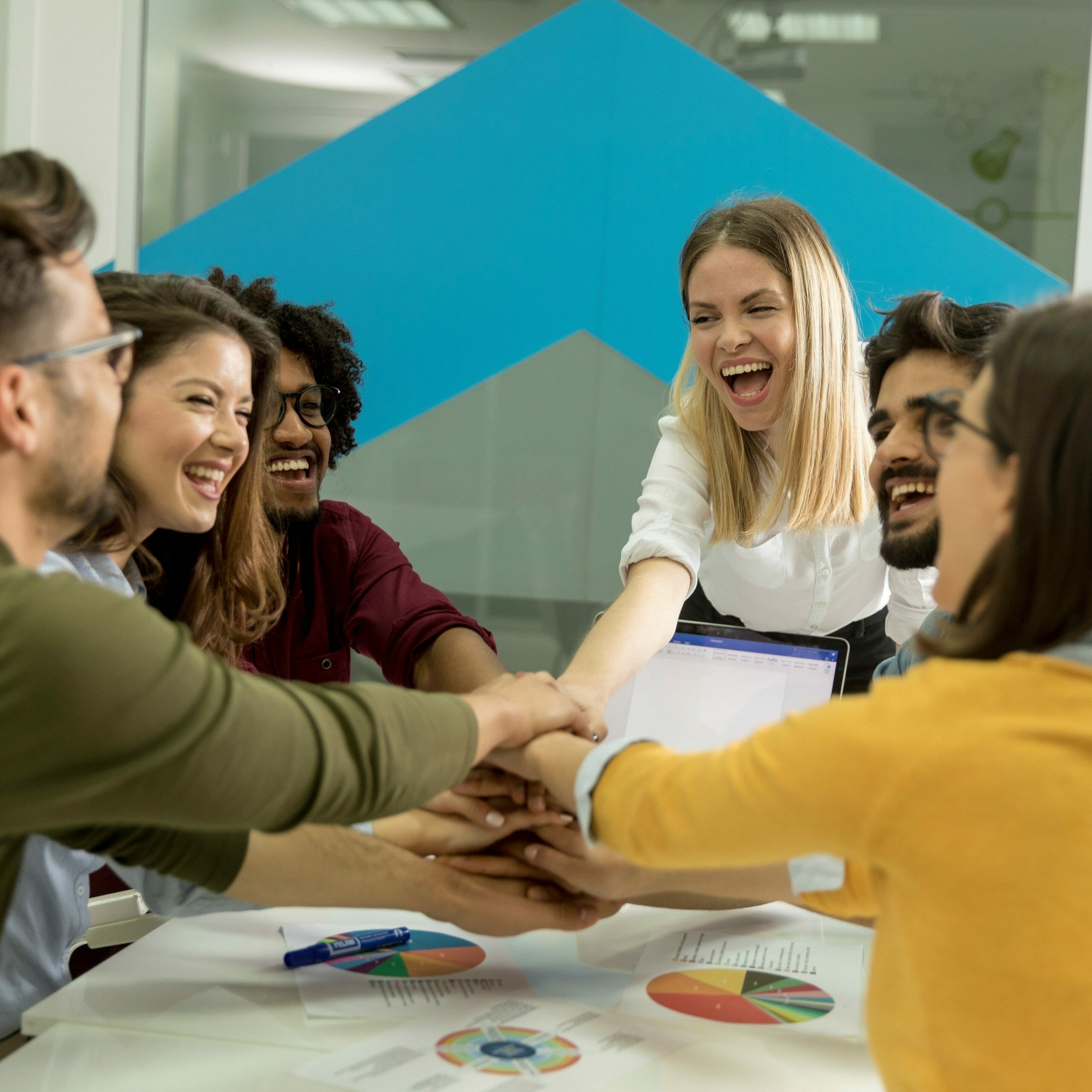 Team of young people stacking hands together over table engaged in teambuilding