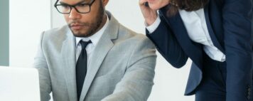 Businesswoman talking to customer on mobile phone. Her male colleague helping her, using laptop and showing screen to her. Business with digital devices concept