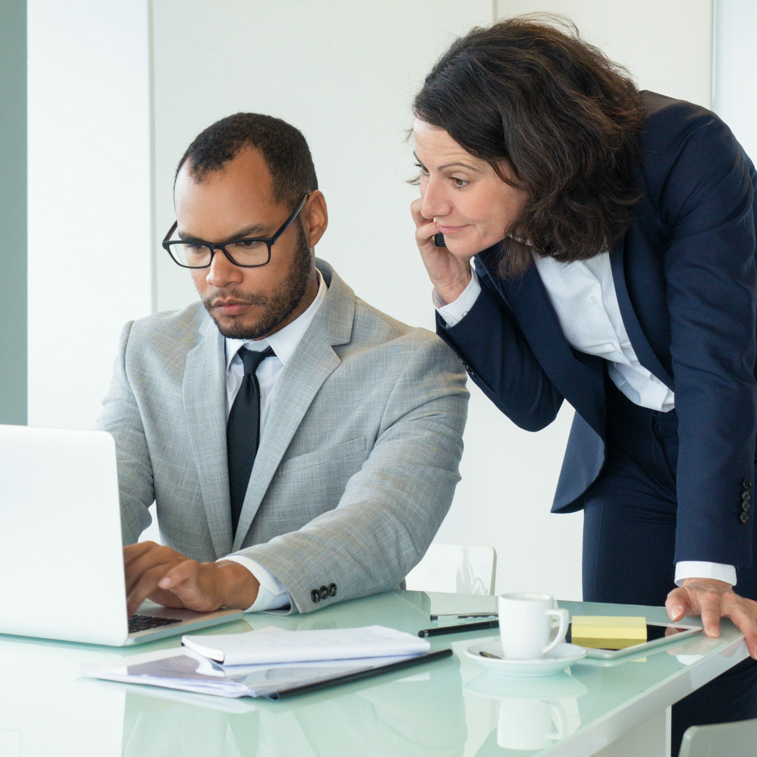 Businesswoman talking to customer on mobile phone. Her male colleague helping her, using laptop and showing screen to her. Business with digital devices concept