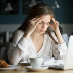 Nervous stressed woman feeling anxiety or strong headache massaging temples studying in cafe, young tired female student experiencing panic attack preparing for test or exam in public place