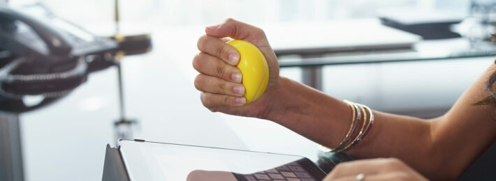 Stressed office worker with anti stress ball types email