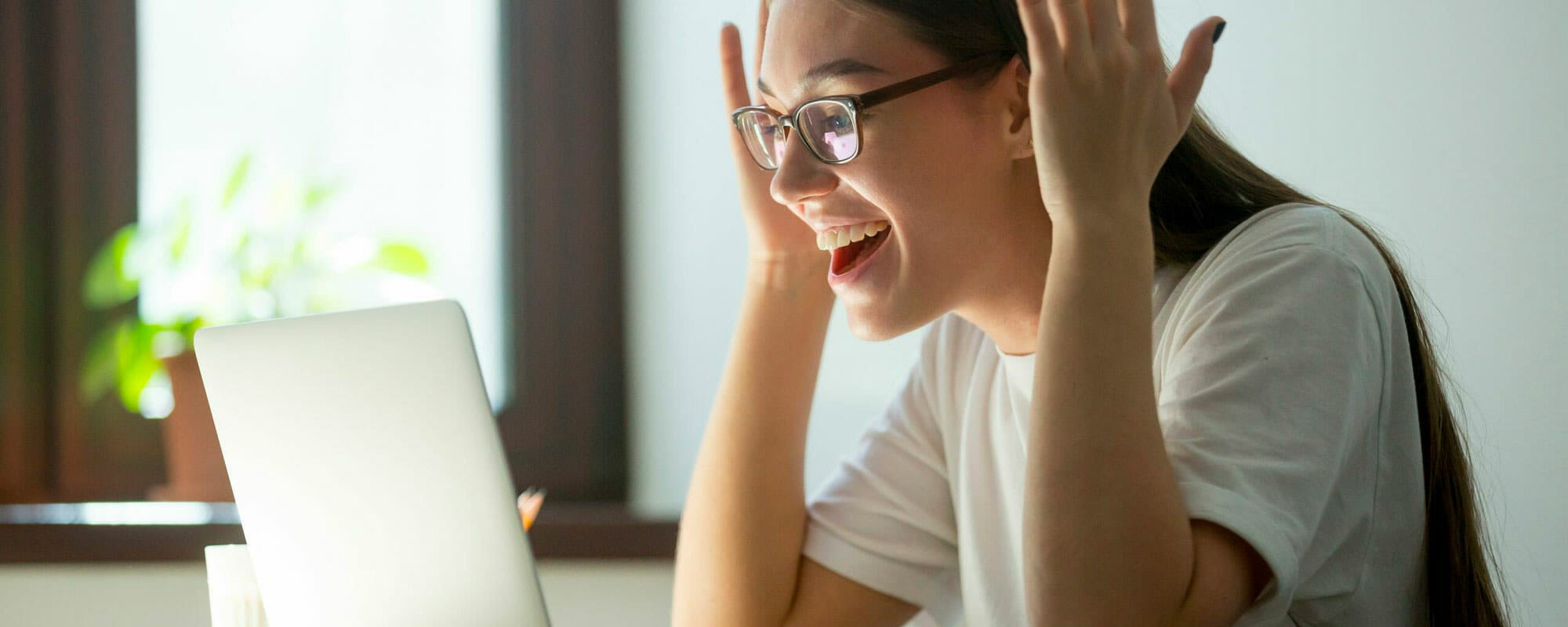 Female student with her hands up looking excited at her laptop