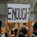 Group of protestors where one individual is holding a sign saying "ENOUGH"