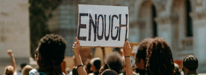 Group of protestors where one individual is holding a sign saying "ENOUGH"