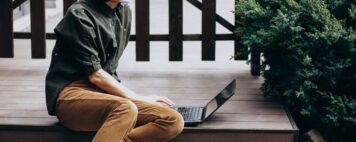 student sitting outside with laptop wearing a face covering