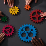 diverse group of individuals pushing colorful gears on a table to each other