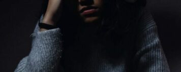 Photo of a woman seated at a desk with a cup of coffee and a distressed expression after having suffered a microaggression