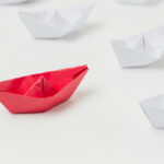 Red paper boat leading white paper boats