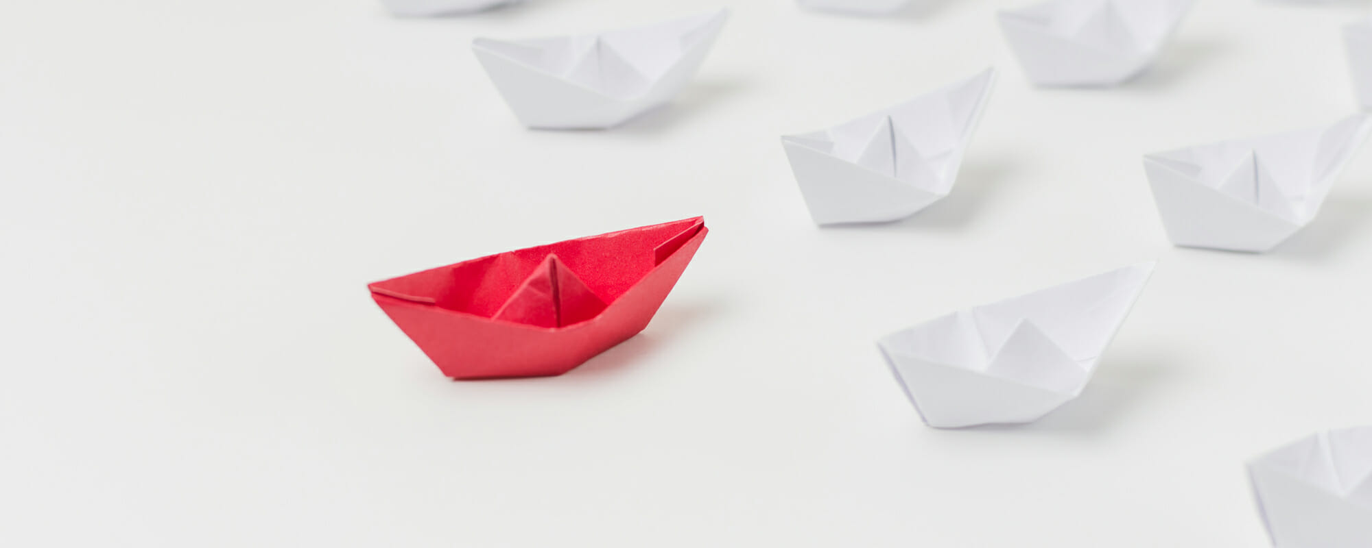 Red paper boat leading white paper boats