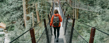 A woman in athletic gear is walking across a bridge towards a platform in a tree.