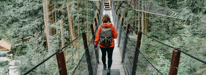 A woman in athletic gear is walking across a bridge towards a platform in a tree.