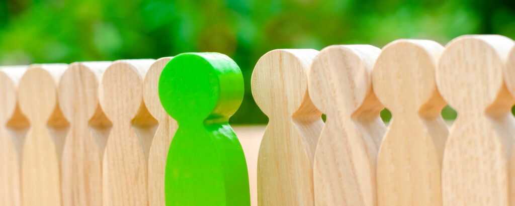 Green wooden figure standing out among other wooden figures