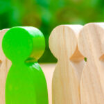 Green wooden figure standing out among other wooden figures