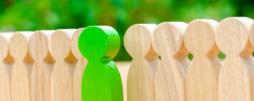 Green wooden figure standing out among other wooden figures