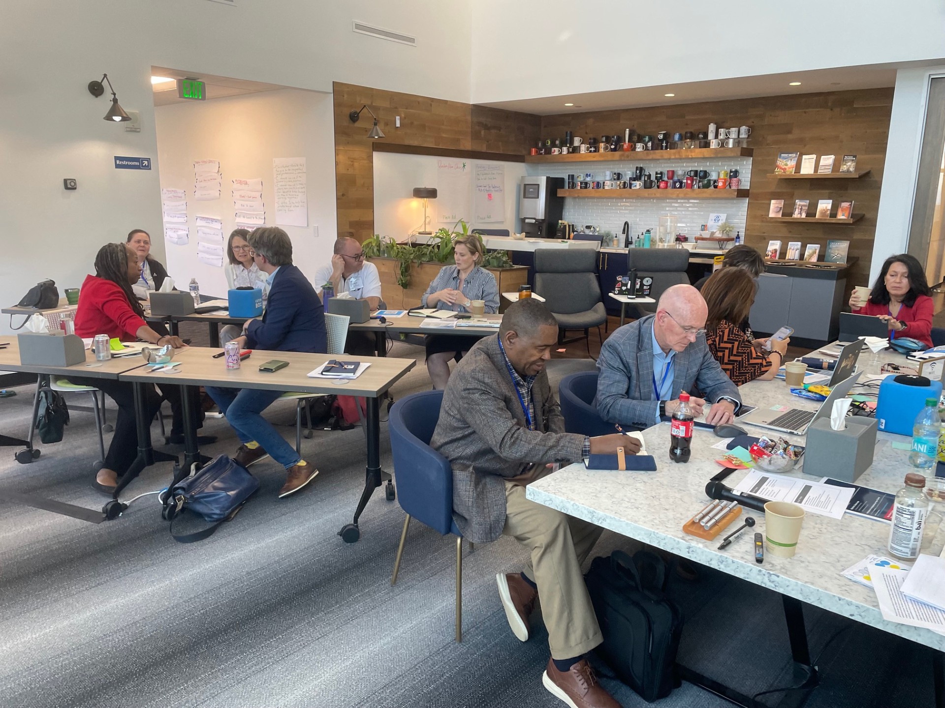 Image depicts an Academic Impressions workshop at their Denver office showing 11 of the attendees taking notes, collaborating, and working on a group activity.